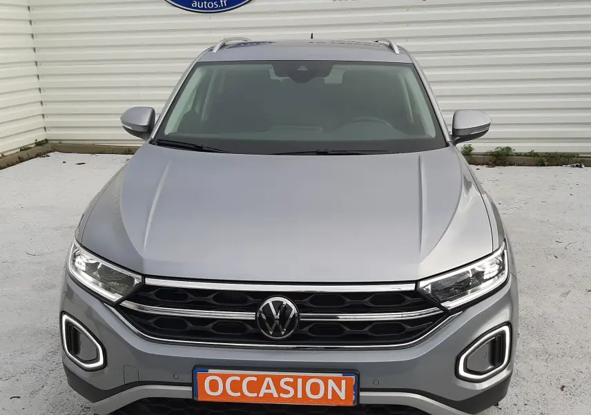 Vue frontale d'un Volkswagen T-Roc gris pyrite 2023 avec calandre noire et feux LED allumés.