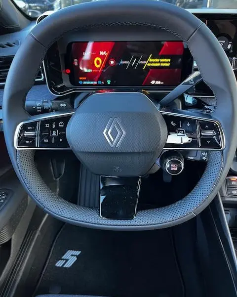 Vue rapprochée du volant noir de la Renault R5 Techno 2024 avec tableau de bord numérique et logo central.