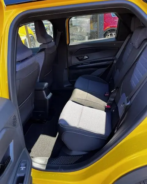 Vue intérieure arrière côté gauche de la Renault R5 Techno jaune 2024, montrant les sièges arrière en tissu gris et noir.