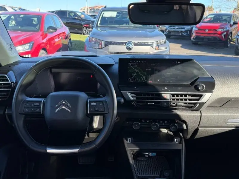 Vue intérieure avant du tableau de bord et volant du Citroën C4 gris acier 2024 avec écran tactile central et commandes au volant.