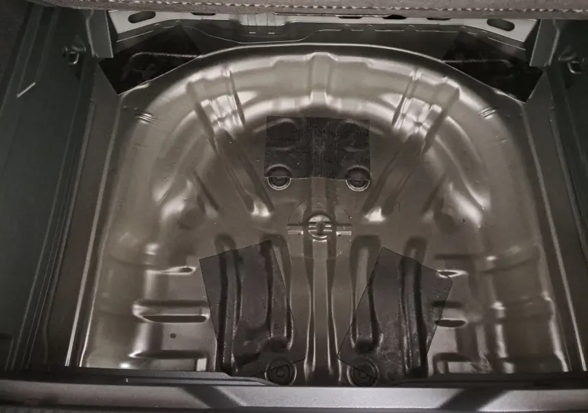 Vue plongeante sur le coffre ouvert du Volkswagen T-Roc noir, montrant la zone de rangement sous le plancher sans roue de secours.