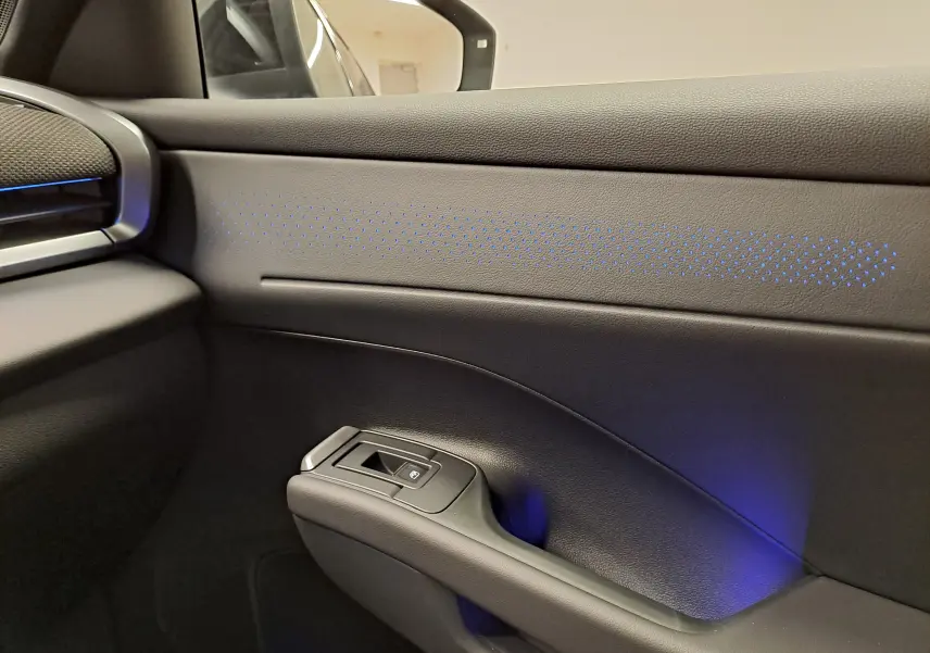Détail de la porte côté passager du Volkswagen T-Roc 2026 noir ébène avec éclairage d'ambiance bleu subtil.