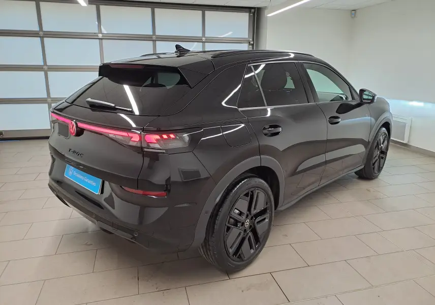 Volkswagen T-Roc 2026 noir ébène en 3/4 arrière droit, jantes noires 19 pouces et feux arrière LED allumés.