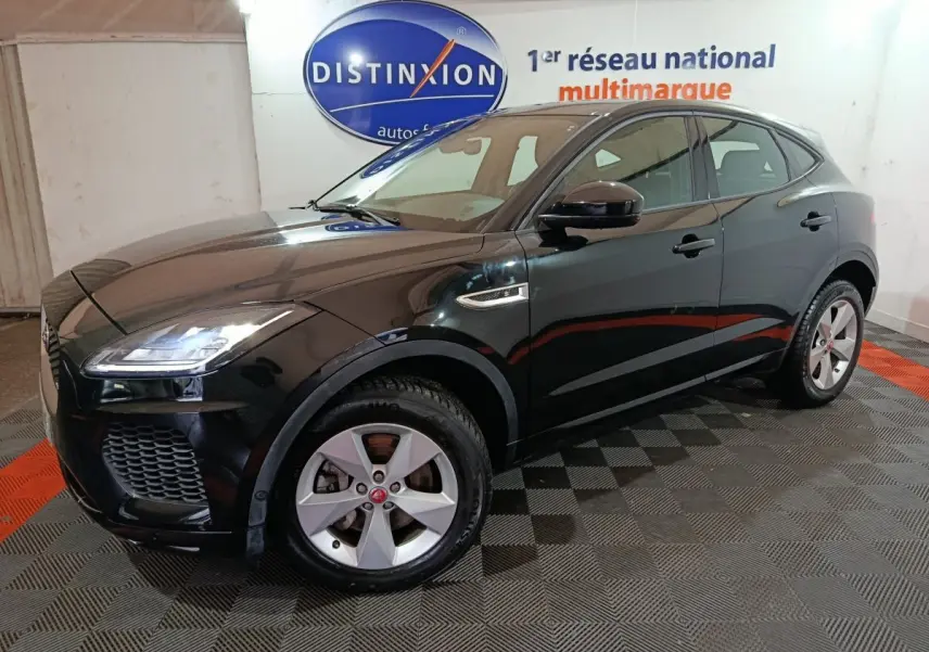 Jaguar E-PACE noir en 3/4 avant droit, avec jantes argentées et phares LED allumés en intérieur showroom.