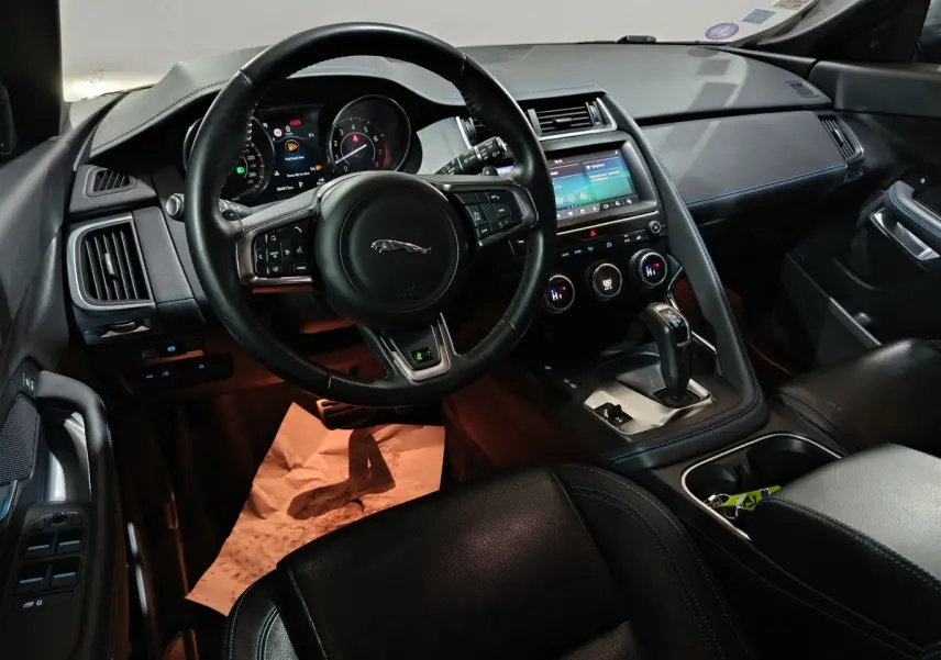 Vue intérieure côté conducteur du Jaguar E-PACE noir, volant cuir multifonctions et écran tactile central visible.