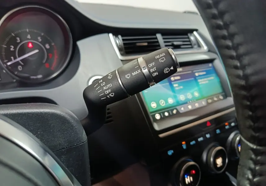 Gros plan sur la commande d’essuie-glace côté gauche du tableau de bord du Jaguar E-PACE noir, avec écran tactile visible.