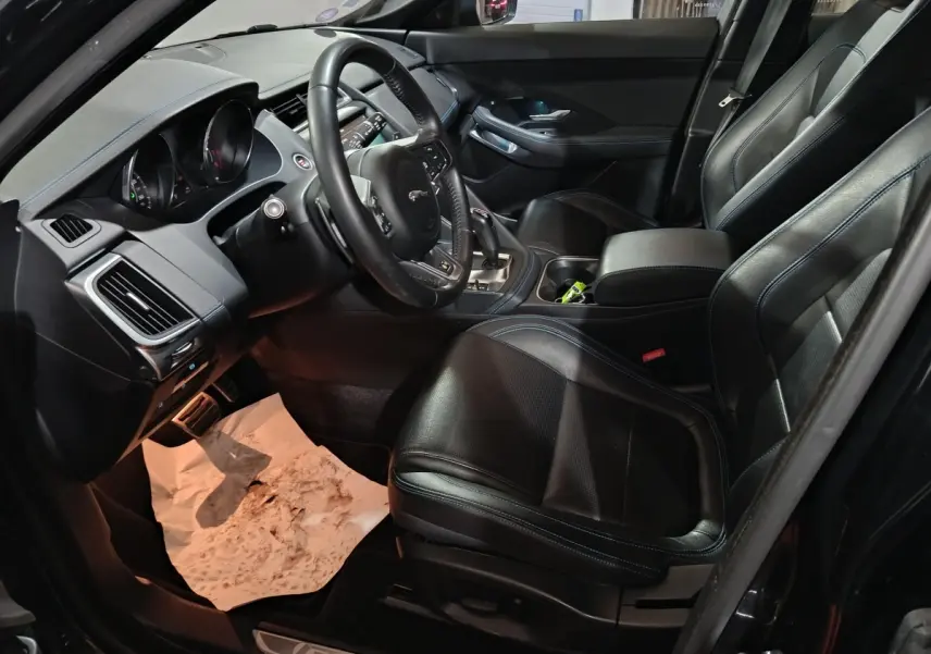 Vue intérieure côté conducteur du Jaguar E-PACE noir, mettant en valeur le volant cuir multifonctions et les sièges sport noirs.