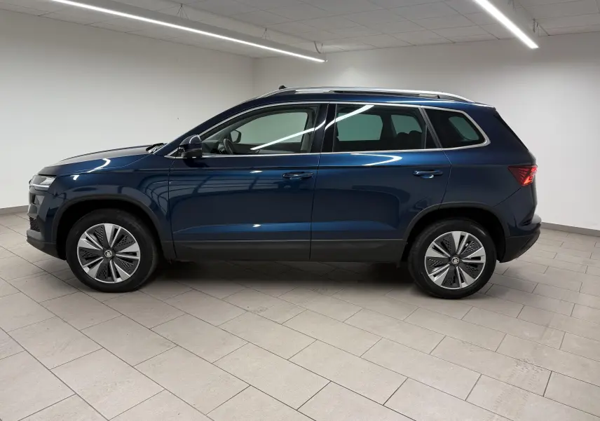 Vue de profil côté gauche d'un Skoda Karoq bleu lave 2023 avec toit ouvrant et attelage, en intérieur.