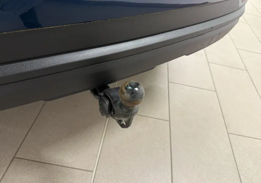 Gros plan sur l'attelage arrière d'un Skoda Karoq 2023 bleu lave, avec pare-chocs noir et sol carrelé visible.