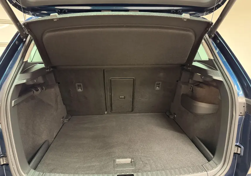 Coffre ouvert vu de l'arrière d'un Skoda Karoq bleu lave 2023, espace de chargement vide et tapis noir.