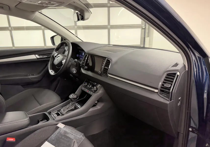 Vue intérieure côté passager du Skoda Karoq bleu lave 2023, montrant tableau de bord et console centrale moderne.