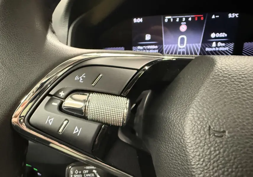 Gros plan sur les commandes gauche du volant du Skoda Karoq 2023, avec tableau de bord numérique en arrière-plan.