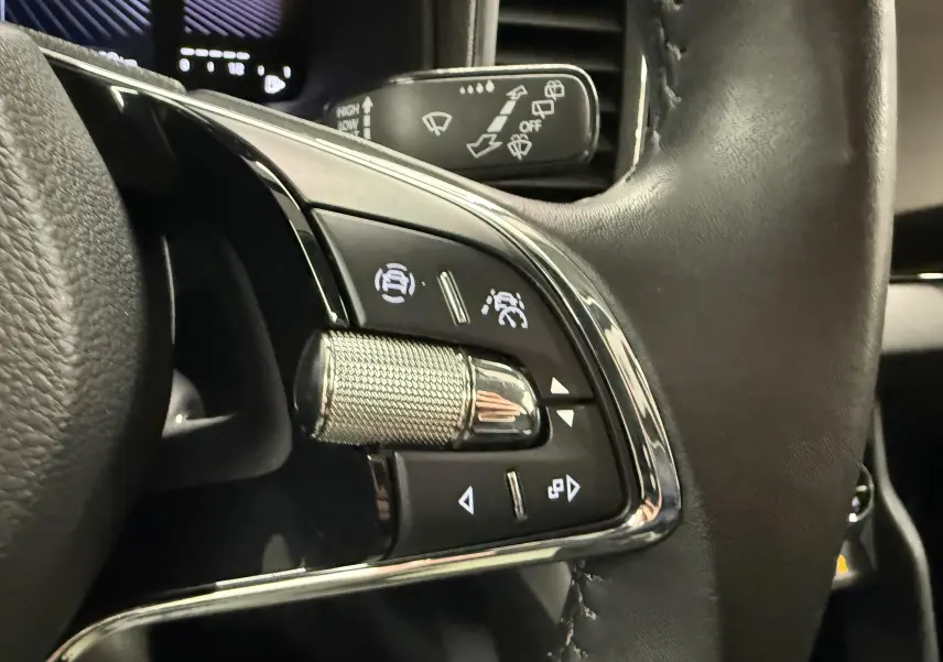 Gros plan sur les commandes du volant en cuir noir du Skoda Karoq 2023, avec molette texturée et boutons lumineux.