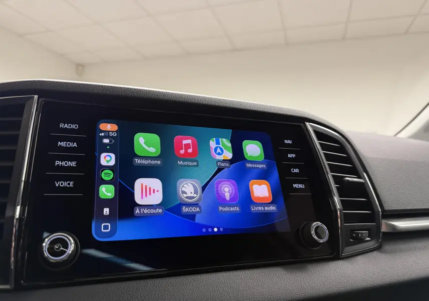 Écran tactile central du Skoda Karoq 2023 affichant Apple CarPlay avec commandes latérales visibles.