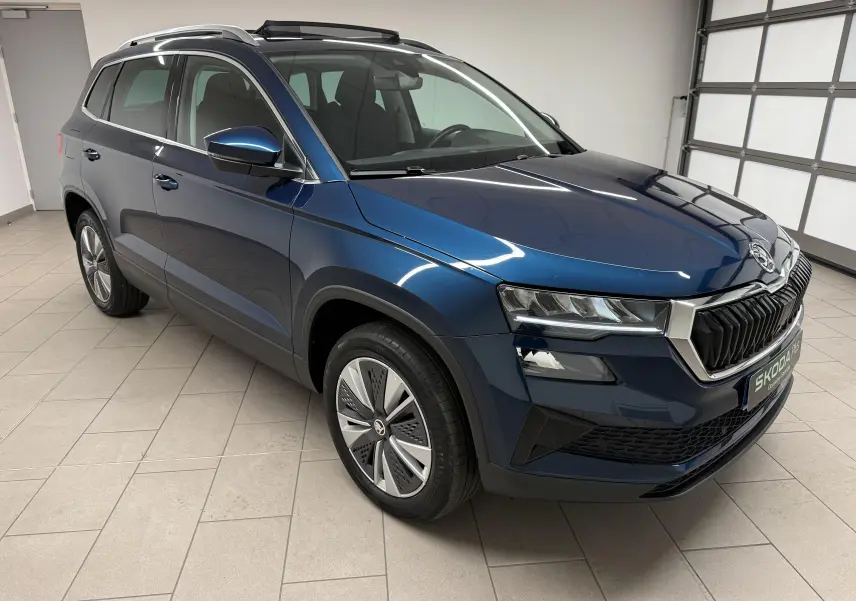Vue 3/4 avant droite du Skoda Karoq bleu lave 2023 avec toit ouvrant et jantes spécifiques en intérieur neutre.