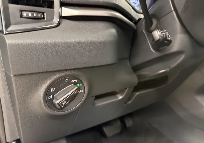 Détail du bouton de commande des phares sur le tableau de bord noir d’un Skoda Karoq 2023 côté gauche.