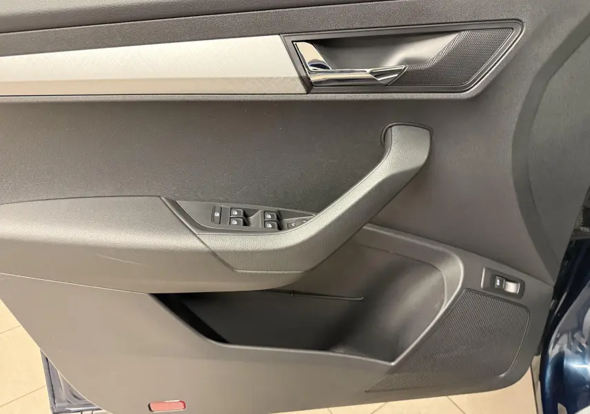 Gros plan sur la porte avant gauche du Skoda Karoq bleu lave, montrant les commandes de vitres et la poignée intérieure chromée.