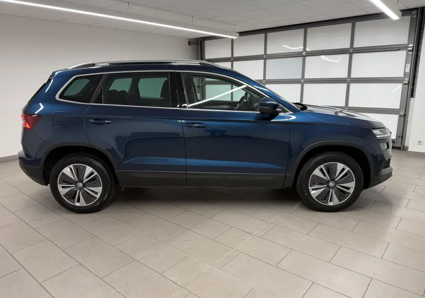 Vue de profil côté gauche d'un Skoda Karoq 2023 bleu lave avec toit ouvrant et jantes spécifiques en intérieur neutre.