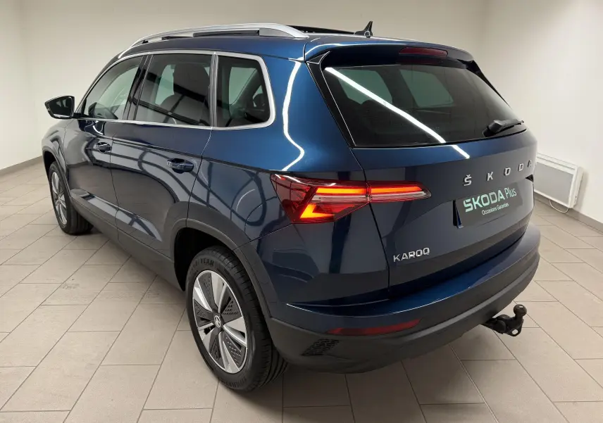 Vue 3/4 arrière droite d'un Skoda Karoq bleu lave 2023 avec attelage et jantes alliage en intérieur showroom.
