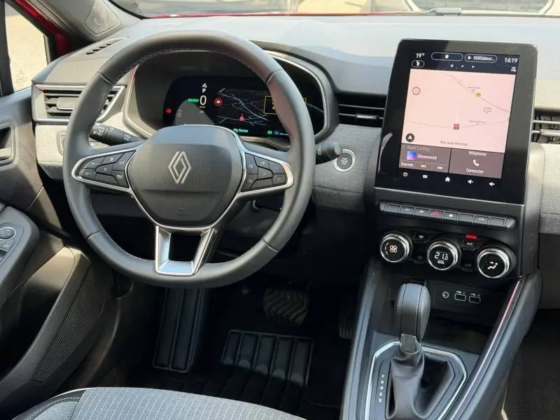 Vue intérieure du poste de conduite de la Renault Clio 1.6 E-Tech 2025, volant multifonction et écran tactile central visible.