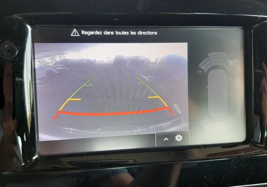 Écran de caméra de recul de la Renault Clio IV noire, affichant les lignes de guidage colorées et l'alerte de sécurité.