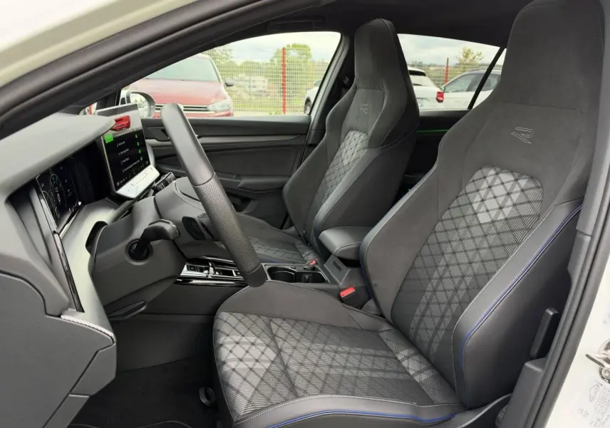 Vue intérieure côté conducteur de la Volkswagen Golf 1.5 eTSI R-Line 2025, sièges sport gris à surpiqûres bleues.