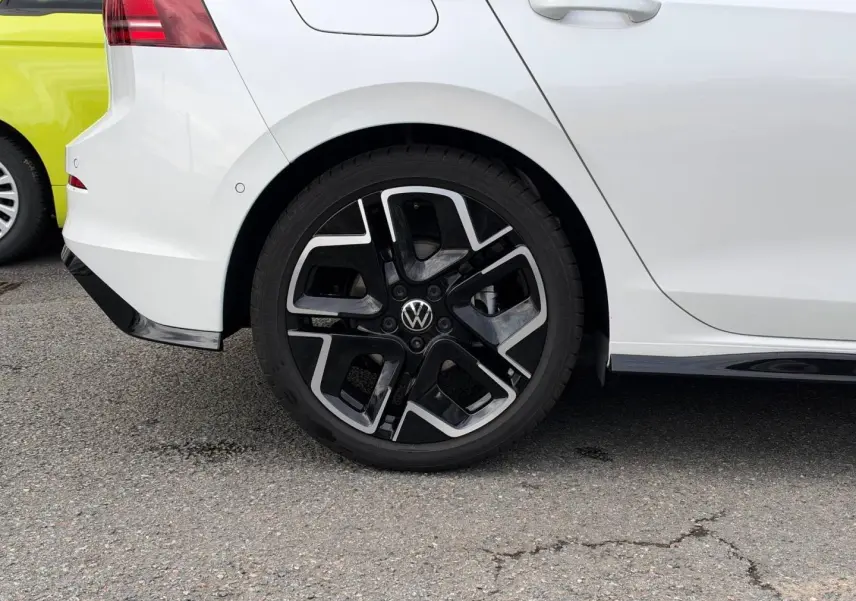Vue latérale droite sur la roue arrière d’une Volkswagen Golf blanche Oryx nacrée avec jante alu noire et argentée.
