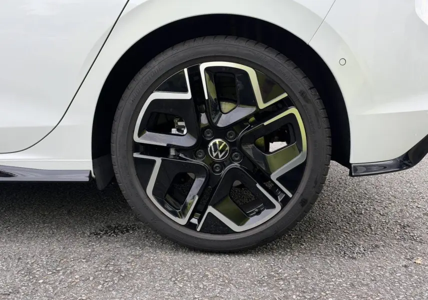 Gros plan sur la roue arrière droite d’une Volkswagen Golf blanche Oryx nacrée avec jante alu noire et argentée R-Line.