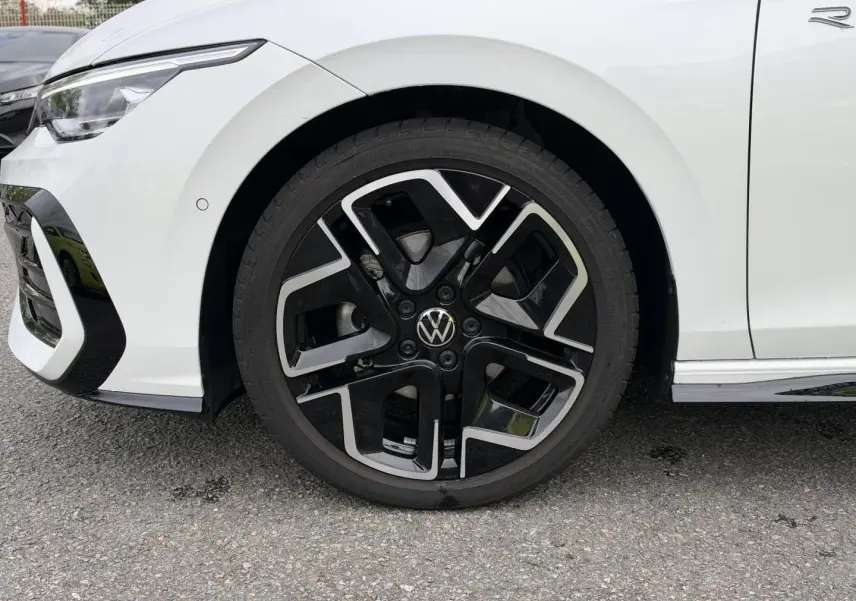 Gros plan sur la roue avant gauche de la Volkswagen Golf blanche Oryx nacrée avec jante alu noire et argentée R-Line.