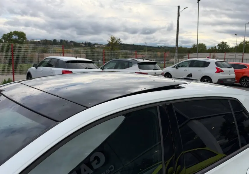 Vue de dessus côté gauche d'une Volkswagen Golf blanche Oryx nacrée avec toit ouvrant panoramique noir partiellement ouvert.
