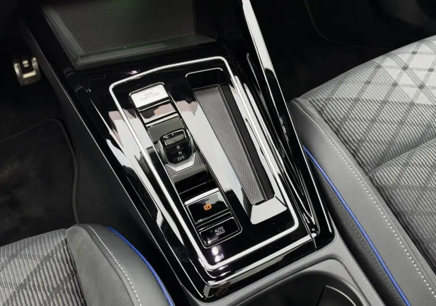 Vue plongeante sur la console centrale brillante avec levier de vitesses électronique et siège tissu gris à surpiqûres bleues de la Volkswagen Golf.