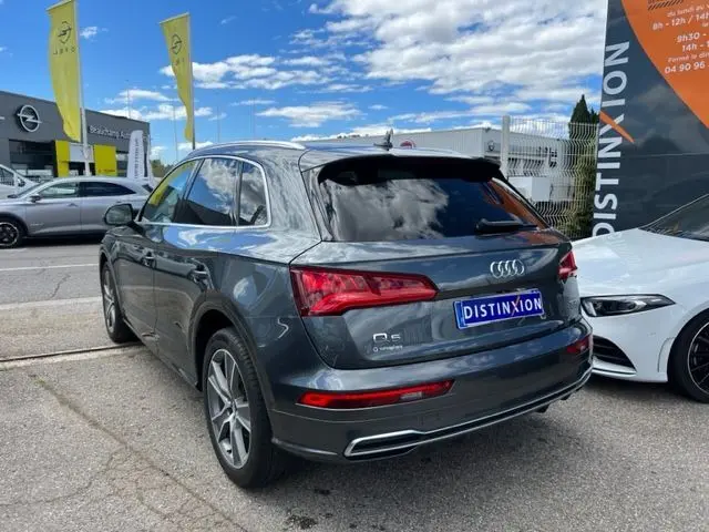 Audi Q5 gris foncé vue 3/4 arrière droit, avec feux LED et badge S Line, stationné devant un concessionnaire.