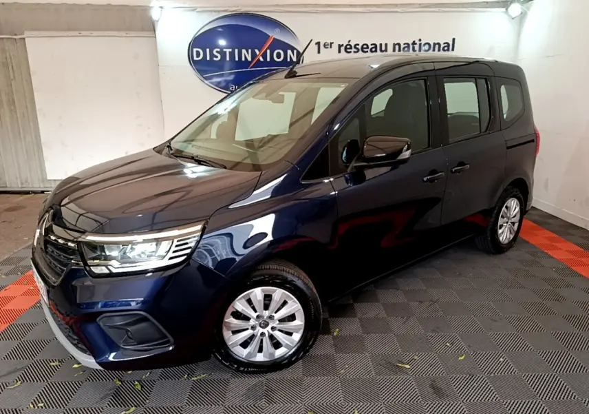 Renault Kangoo Equilibre TCe 100 bleu en 3/4 avant droit, avec phares LED et jantes alliage visibles en intérieur showroom.