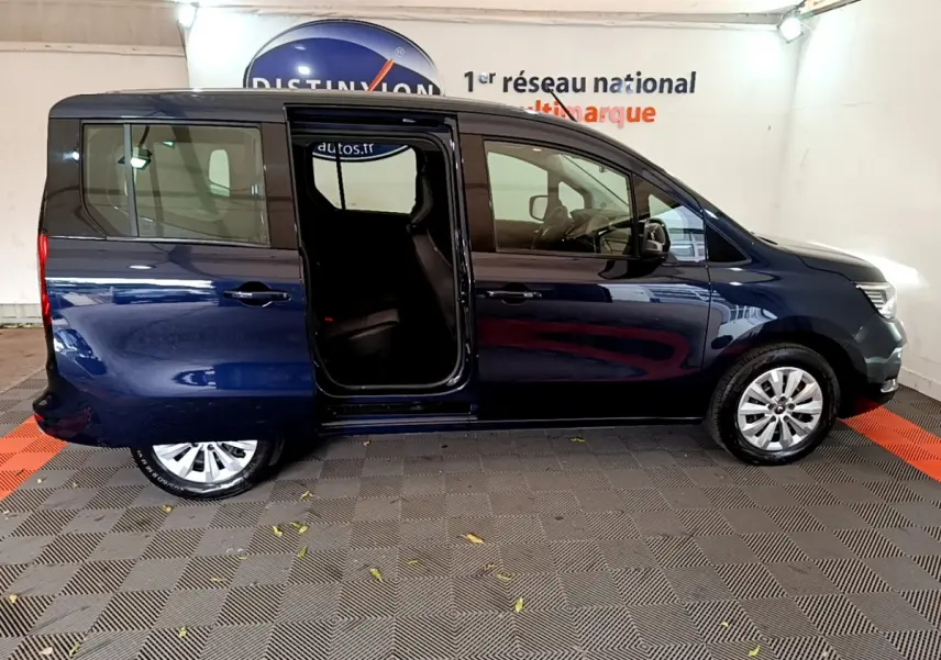 Profil droit d’un Renault Kangoo bleu 2023 avec porte coulissante arrière ouverte, stationné en intérieur.