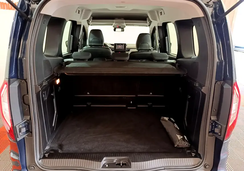 Vue arrière du coffre ouvert d'un Renault Kangoo bleu 2023, montrant l'intérieur spacieux et la tablette de séparation.