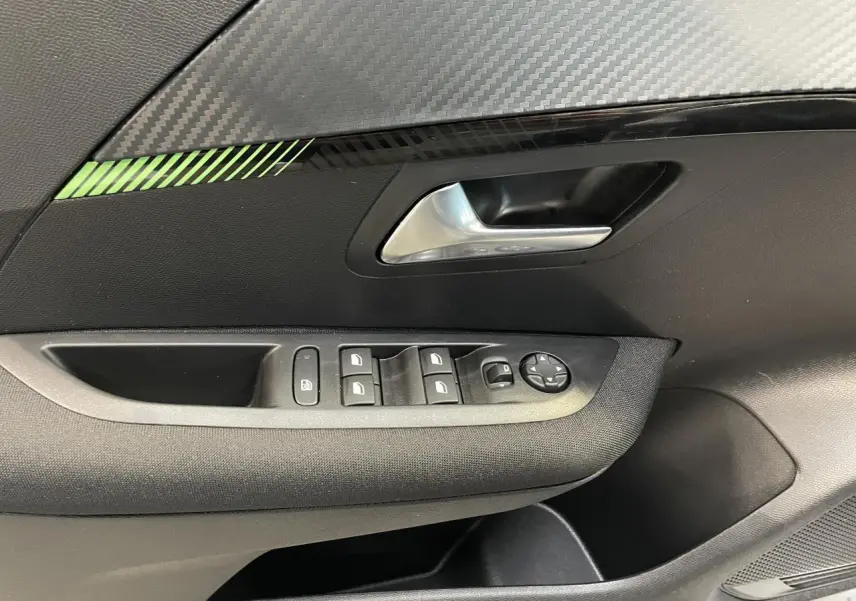 Détail de la porte avant gauche de la Peugeot 208 2024, avec commandes de vitres et décor carbone vert.