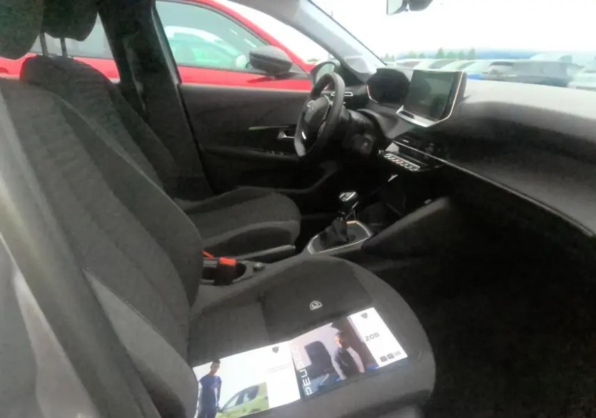 Vue intérieure côté conducteur de la Peugeot 208 gris clair 2024 avec tableau de bord et écran tactile central.
