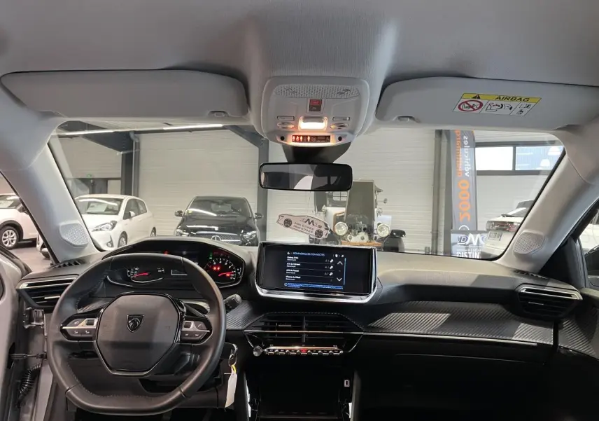 Vue intérieure avant du tableau de bord et volant noir de la Peugeot 208 1.2i PureTech 2024 avec écran tactile central.