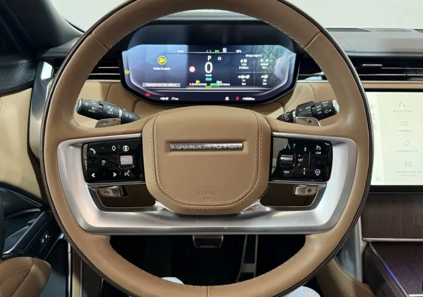 Vue rapprochée du volant cuir beige du Range Rover PHEV 2024 avec tableau de bord numérique et commandes intégrées.
