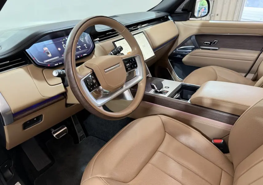 Intérieur beige du Range Rover PHEV 2024 vu côté conducteur, avec tableau de bord digital et volant cuir bois.