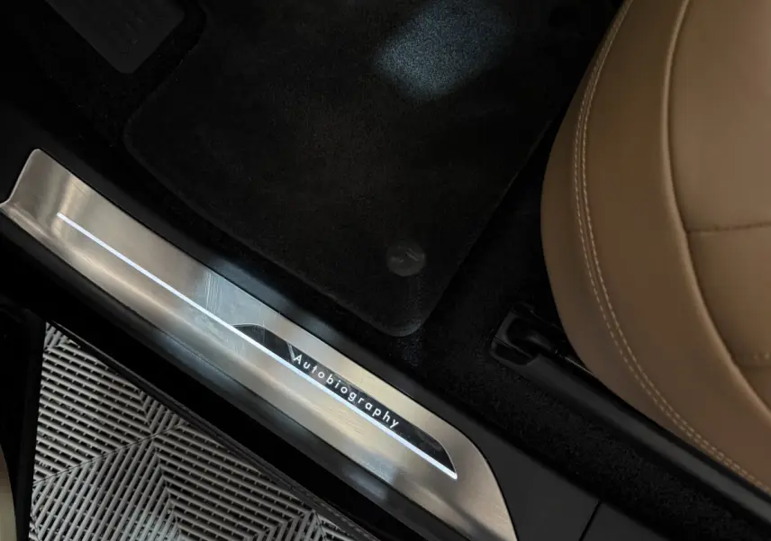 Détail intérieur montrant la plaque de seuil de porte "Autobiography" sur un Range Rover noir avec siège cuir beige.