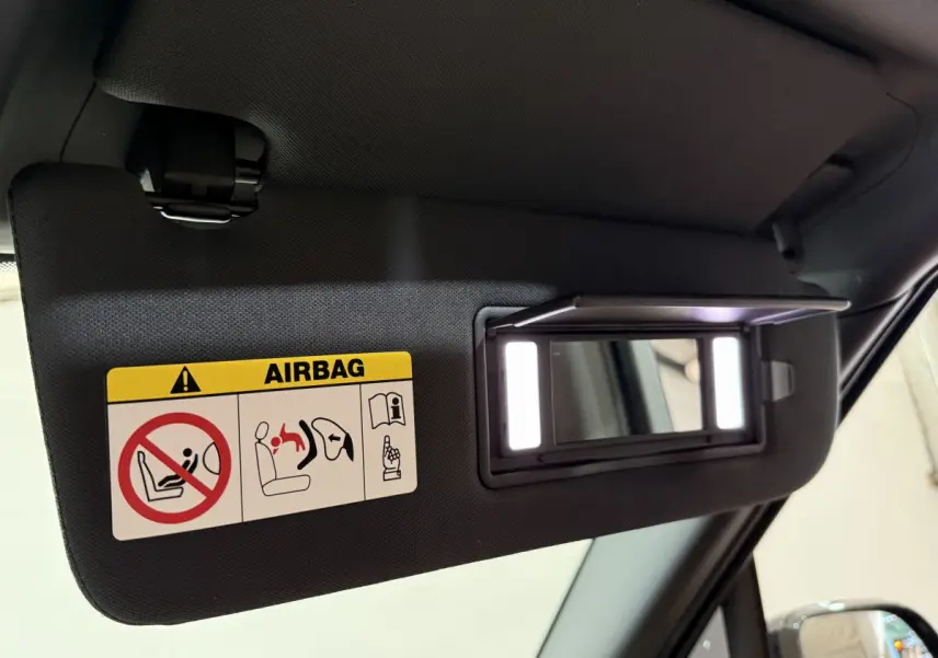 Pare-soleil côté conducteur noir avec miroir éclairé et étiquette airbag, intérieur d'un Range Rover PHEV 2024 noir.