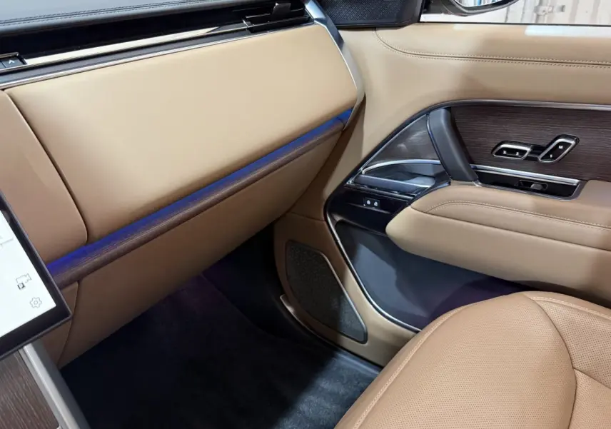 Intérieur côté passager du Range Rover PHEV noir 2024, avec sellerie beige et inserts bois sur la porte.
