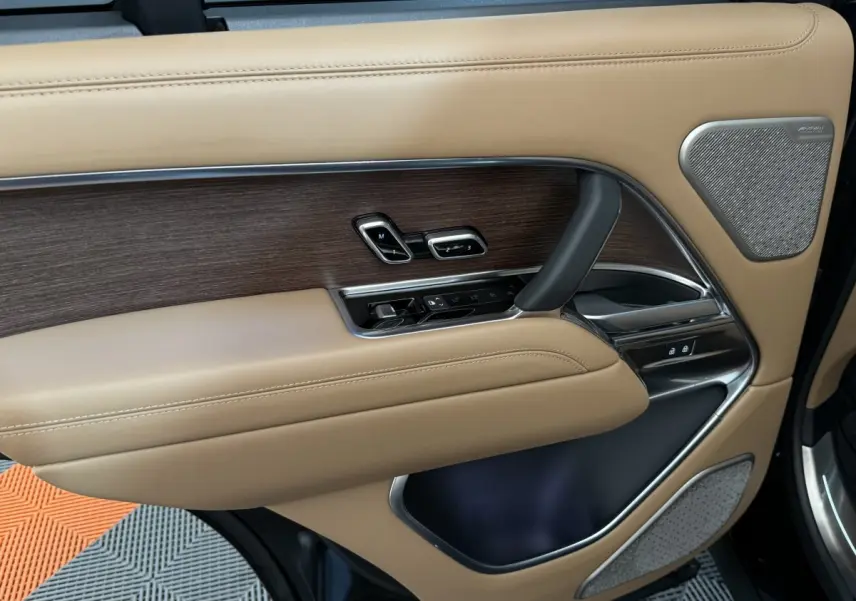 Gros plan sur la porte intérieure côté gauche du Range Rover PHEV 2024, cuir beige et inserts bois avec commandes électriques.