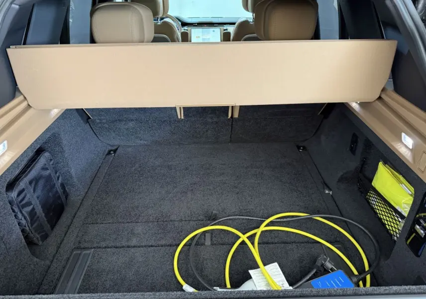 Coffre ouvert d’un Range Rover PHEV noir, vue arrière montrant la moquette noire et un câble de recharge jaune.