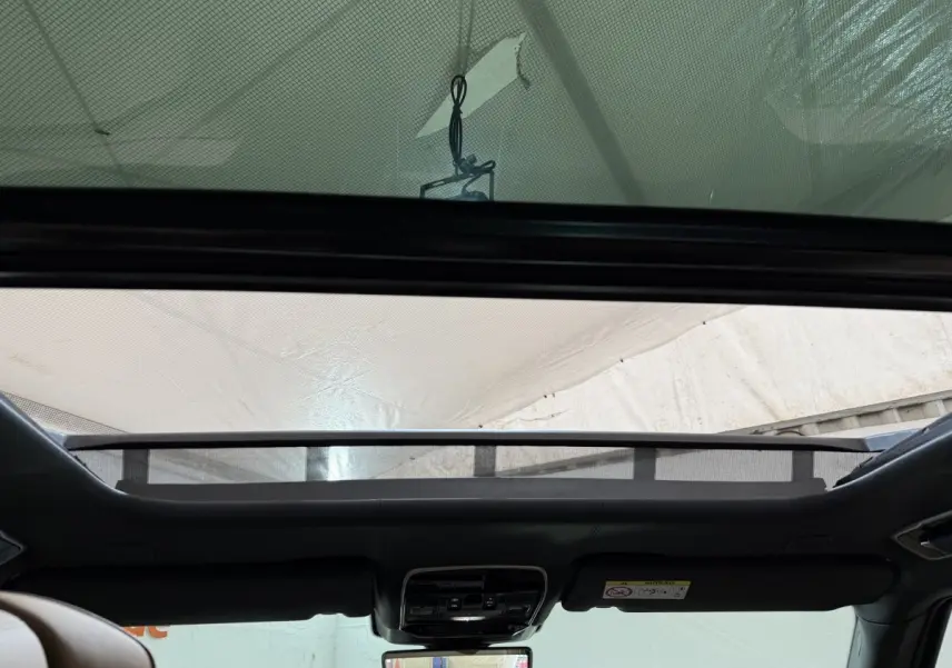 Vue intérieure vers le toit ouvrant en verre du Range Rover PHEV P550e noir, avec commandes et rétroviseur central visibles.