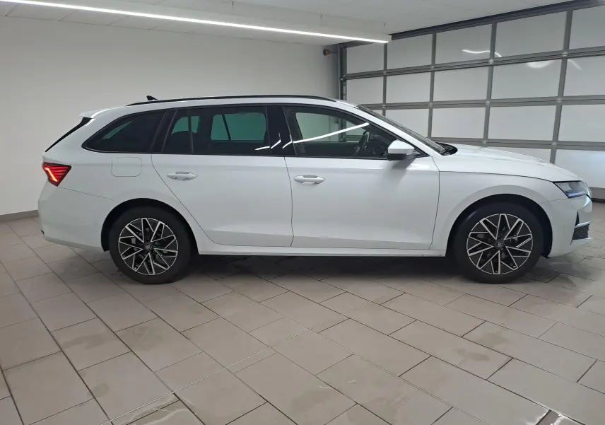 Vue de profil droit d’une Skoda Octavia Combi 2025 blanche Moon avec jantes alliage noires polies dans un garage.