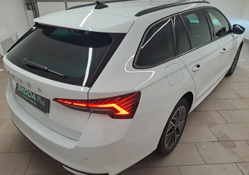 Vue 3/4 arrière droite d'une Skoda Octavia Combi blanche Moon avec feux arrière allumés et jantes alliage noires polies.