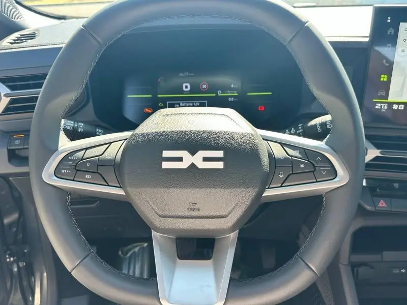 Vue rapprochée du volant multifonction noir et gris du Dacia Bigster 2025 avec tableau de bord numérique en arrière-plan.