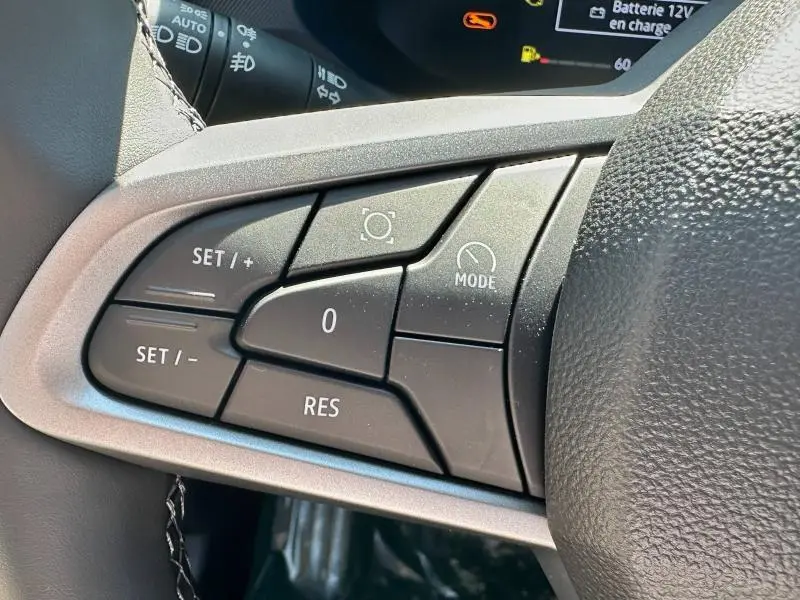 Gros plan sur les commandes multifonctions noires à gauche du volant du Dacia Bigster blanc, avec marquages blancs.